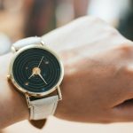 round gold colored black analog watch with grey leather band